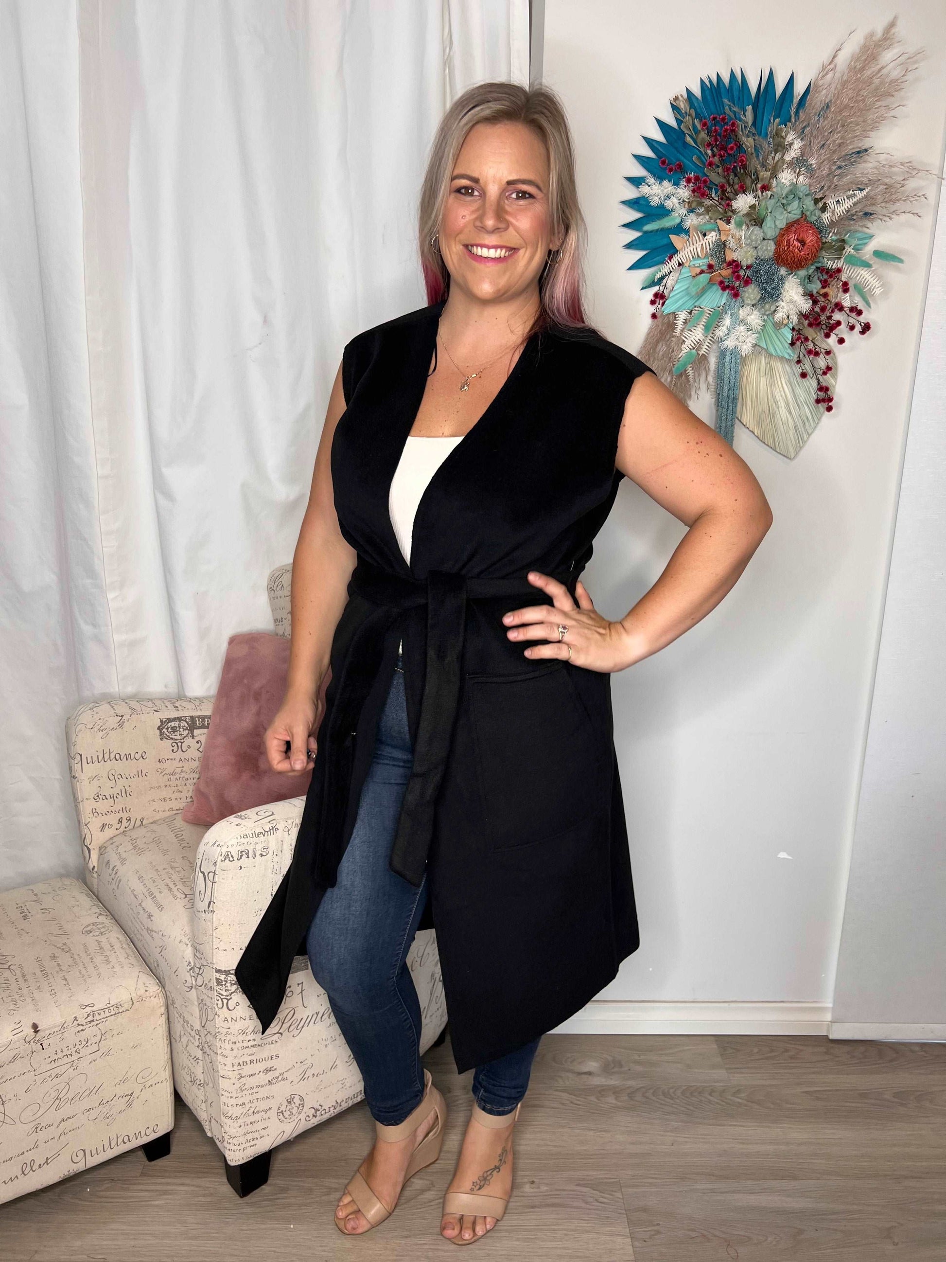 Alica Belted Sleeveless Coat - Black | Betty Basics | Are you ready to add a touch of elegance to your autumnal layering game? Look no further than the Alicia Belted Sleeveless Coat! This piece is the perfect combinatio